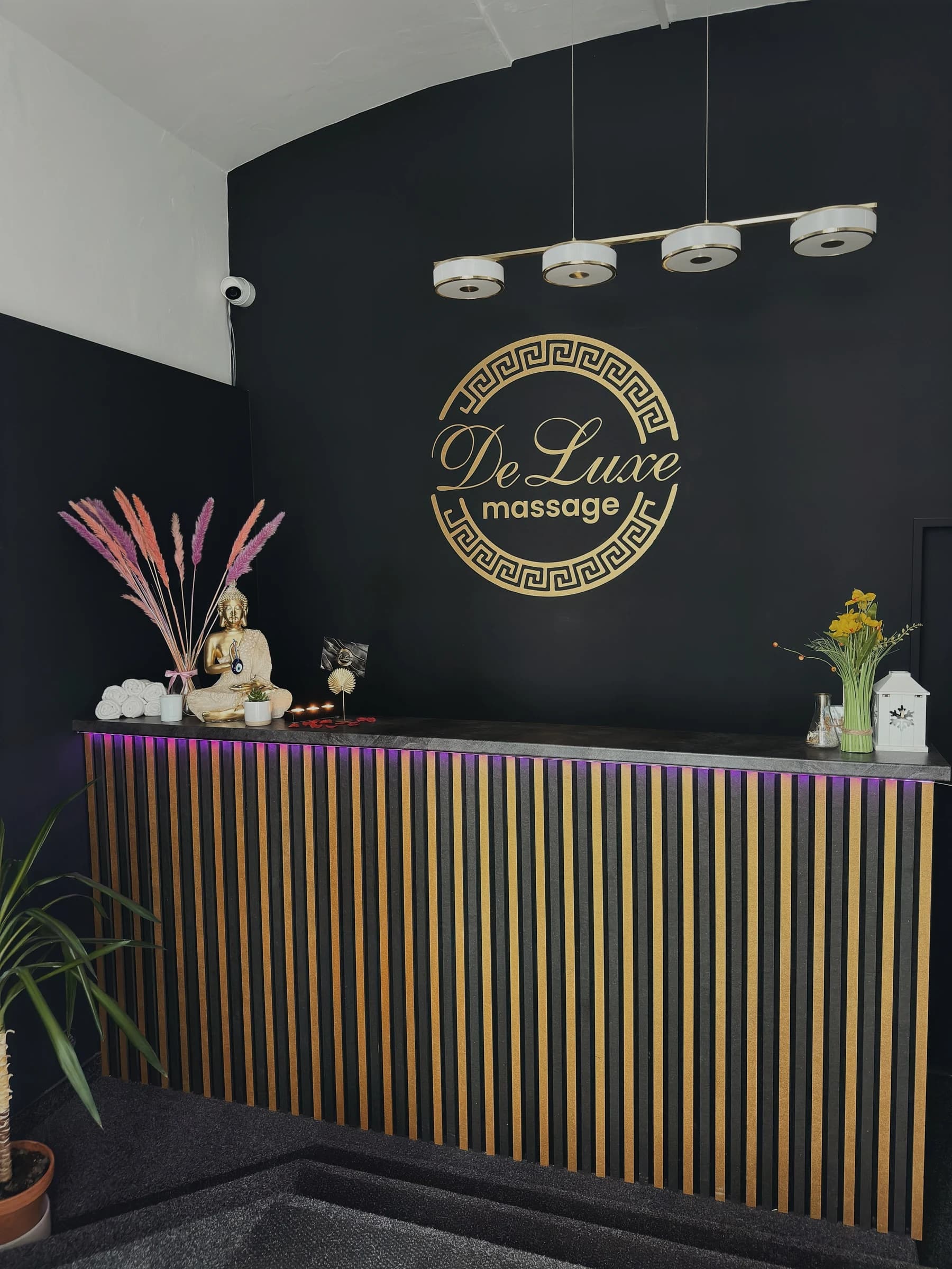 Zvětšit fotografii: Recepce salonu: zlat� logo DeLuxe massage na �ern� st�n� a pult se zlat�mi lamelami