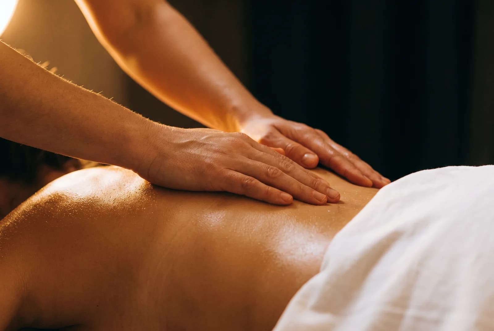 Enlarge photo: A therapist working the back and neck muscles of a client lying under a gold drape