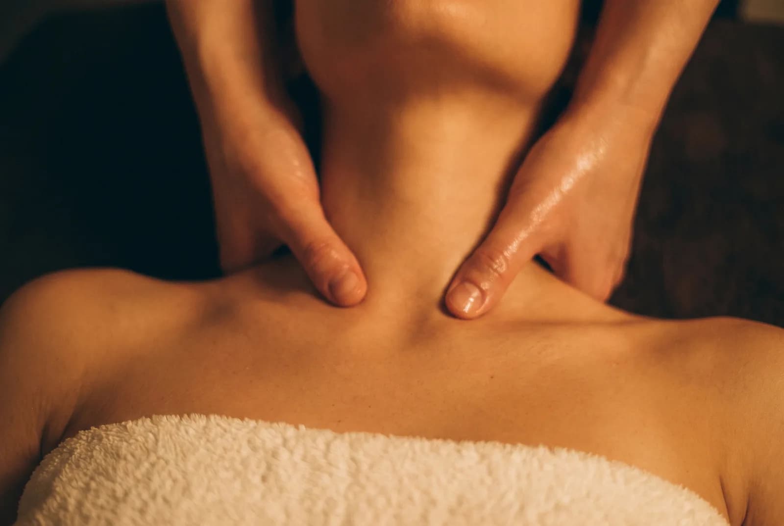 Enlarge photo: A therapist working the back and neck muscles of a client lying under a gold drape
